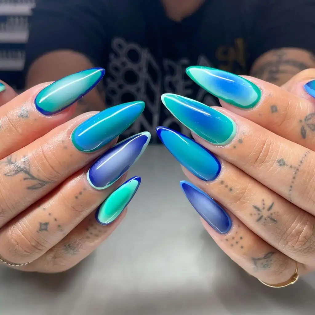 Blue and green ombre almond nails on a tattooed hand