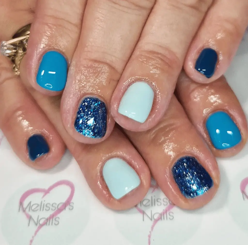 Short blue, navy, and glitter nails in a mismatched pattern