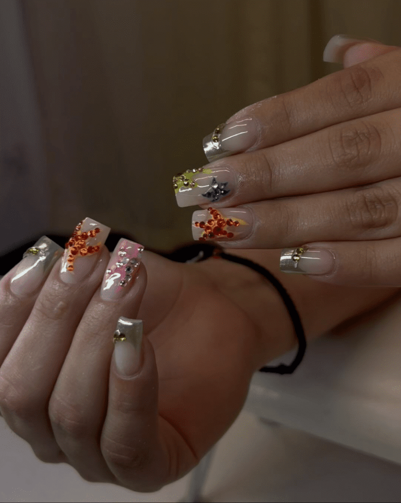 Clear nude nails with silver chrome tips and orange rhinestone accents