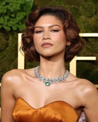 Short curly auburn bob styled with a diamond and emerald necklace